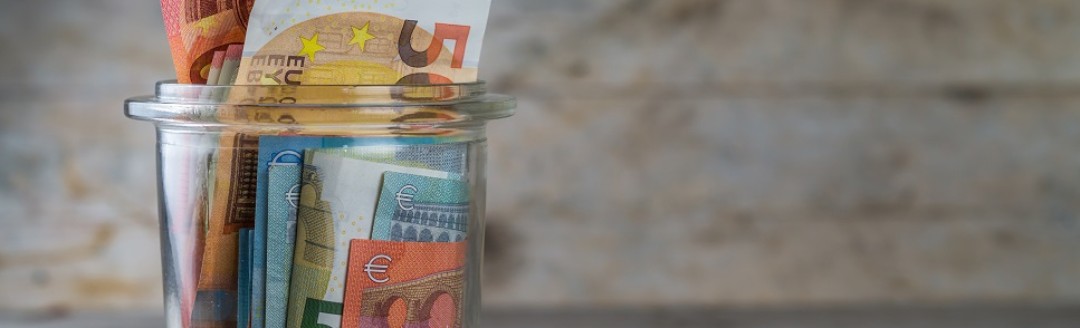 Ein durchsichtiges Glas mit diversen Geldscheinen befüllt. 