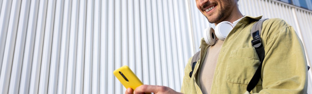 Ein junger Mann schaut beim Gehen lächelnd auf sein Handy