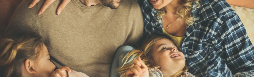 Ein junger Mann und eine junge Frau liegen Arm in Arm. Zwei junge Mädchen liegen auf ihren Schößen. 