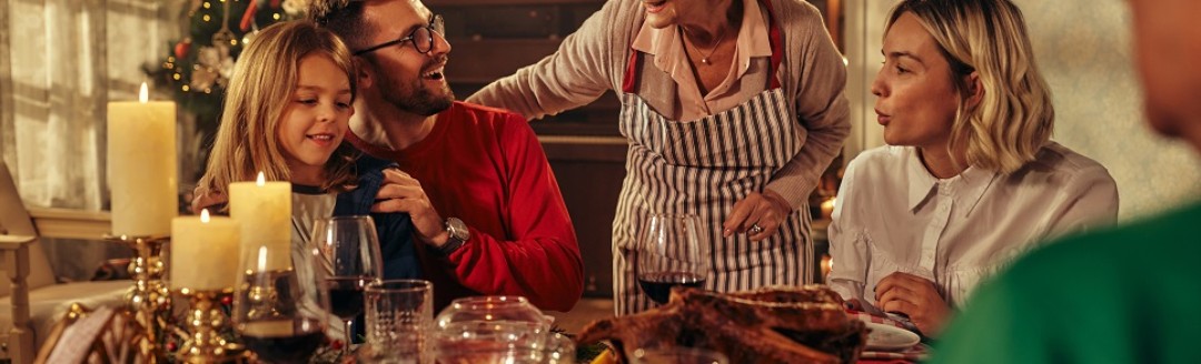 Eine Familie sitzt zusammen am Weihnachtstisch und isst. Drum herum ist es weihnachtlich geschmückt. 