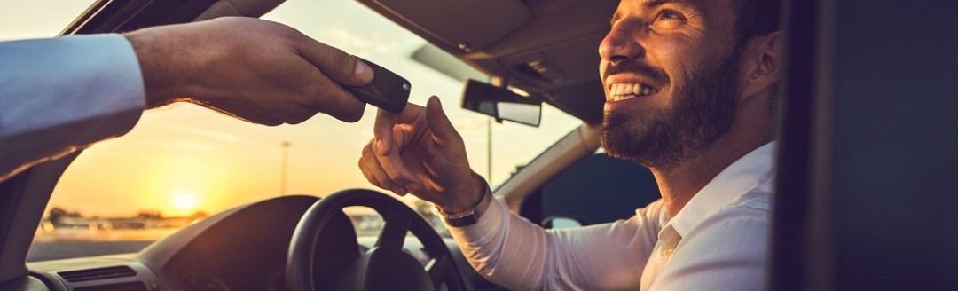 Ein Mann sitzt am Steuer eines Auto und ihm werden die Autoschlüssel gereicht. 