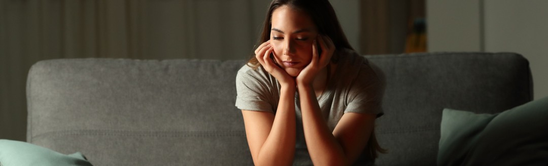 Eine junge Frau sitzt in ihrem Wohnzimmer ohne Strom und schaut ernüchternd auf drei leuchtende Kerzen auf dem Wohnzimmertisch. 