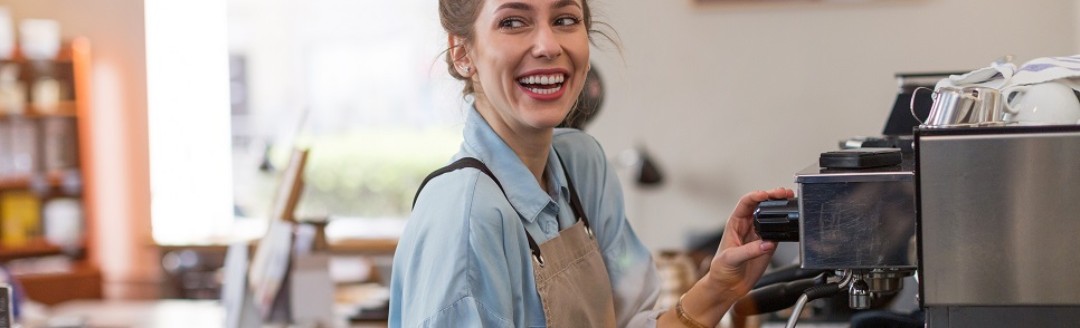 Eine junge Frau bereitet als Barista einen Kaffee an einer Kaffeemaschine in einem Café zu. 