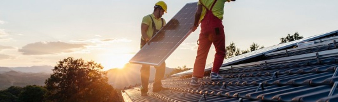 Zwei Bauarbeiter bringen eine Solaranlage auf einem Dach an.