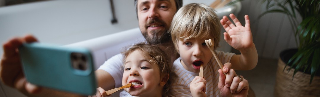 Ein Vater nimmt mit seiner Tochter und seinem Sohn ein Selfie auf, während sie beide am Zähne putzen sind.