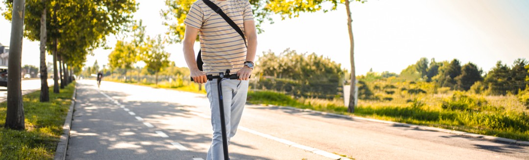Mann trägt Schutzhelm beim Fahren mit seinem E-Scooter.