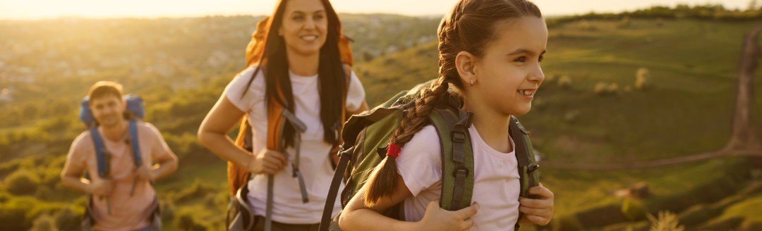 Eine junge Familie geht im Sonnenschein wandern. Die junge Tochter steht im Vordergrund.