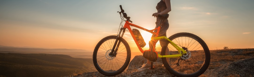 Eine Frau sitzt auf ihrem E-Bike auf einem Berg im Sonnenuntergang. 