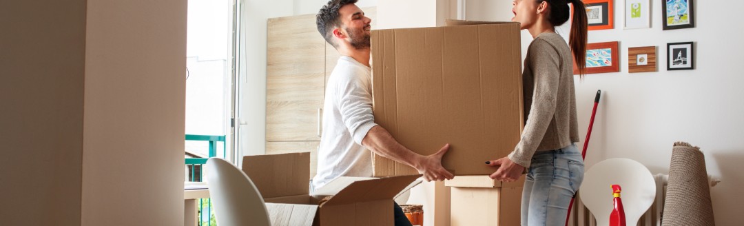 Ein Paar trägt zusammen einen Karton durch das Wohnzimmer.