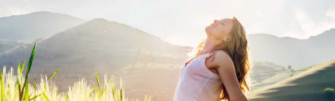 Eine Frau steht inmitten eines gelben Feldes und schaut in die Sonne