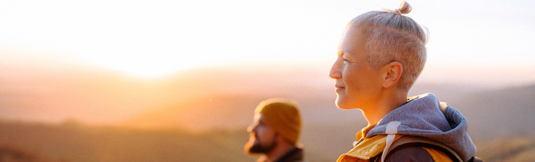 Eine Frau und ein Mann stehen in goldenem Licht in der Landschaft und schauen nach links.