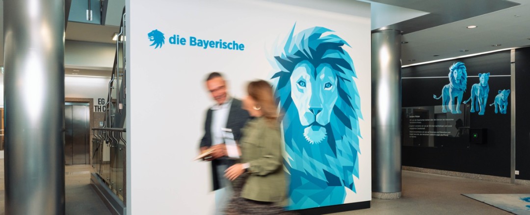 Eine Mitarbeiterin und ein Mitarbeiter der Bayerischen laufen gemeinsam durchs Foyer der Bayerischen