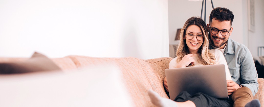 Zwei Personen sitzen auf einem Sofa und schauen gemeinsam auf einen Laptop.