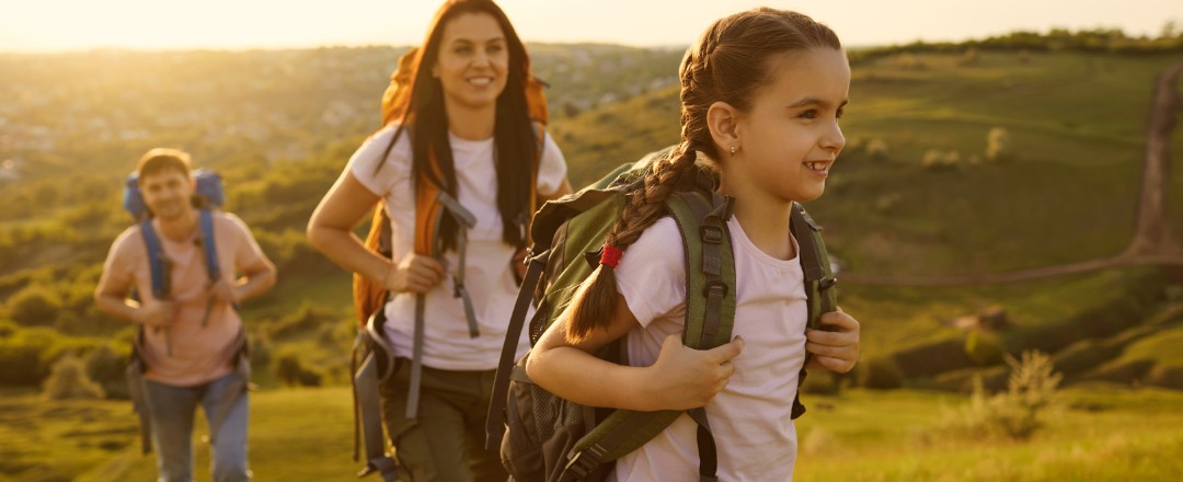 Eine junge Familie geht im Sonnenschein wandern. Die junge Tochter steht im Vordergrund.