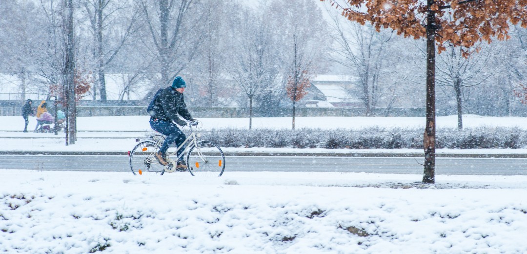 Ein Mann fährt im Schnee und durch einen leichten Schneesturm sein Fahrrad. 