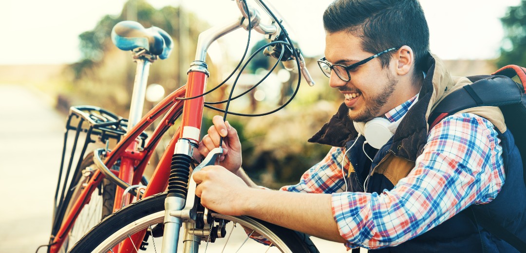 Eine Person repariert im Freien ein rotes Fahrrad und verwendet dabei ein Werkzeug an der Vordergabel.