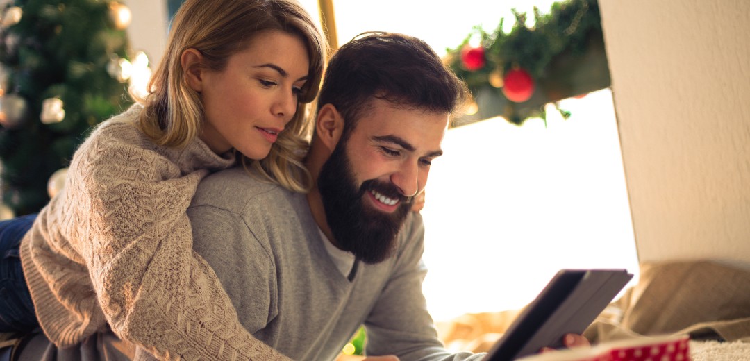 Ein Pärchen schaut zusammen in ein Tablet. Die Umgebung schaut weihnachtlich aus.