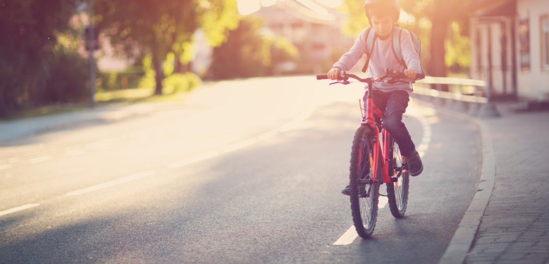 Ein junges Kind fährt mit seinem Fahrrad den Fahrradstreifen auf einer Straße entlang. 