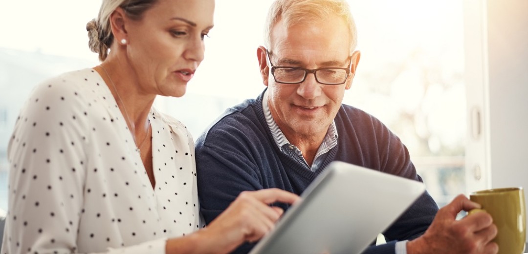 Ein Mann und eine Frau schauen gemeinsam auf ein Tablet und besprechen etwas. 
