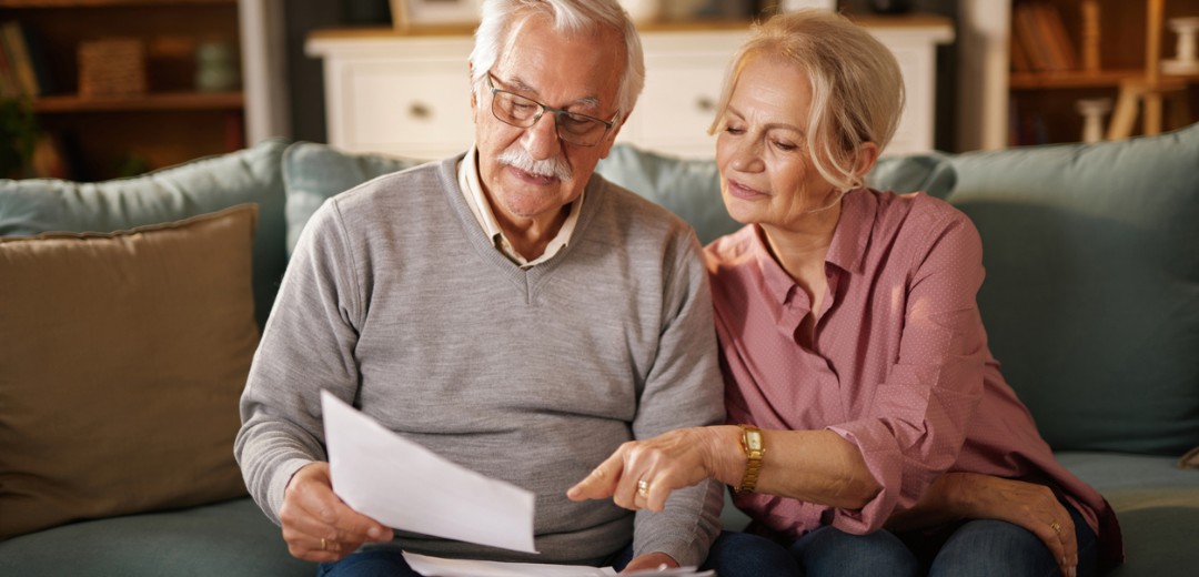 Älteres Paar sitzt auf dem Sofa und schaut gemeinsam Dokumente durch.