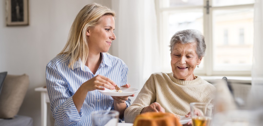 Eine erwachsene und eine ältere Frau sitzen zusammen für Tee und Kuchen. 
