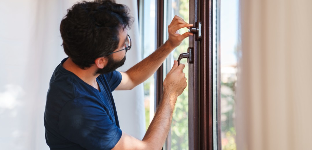 Ein Mann verschließt ein Fenster und trifft Vorkehrungen gegen einen Einbruch.