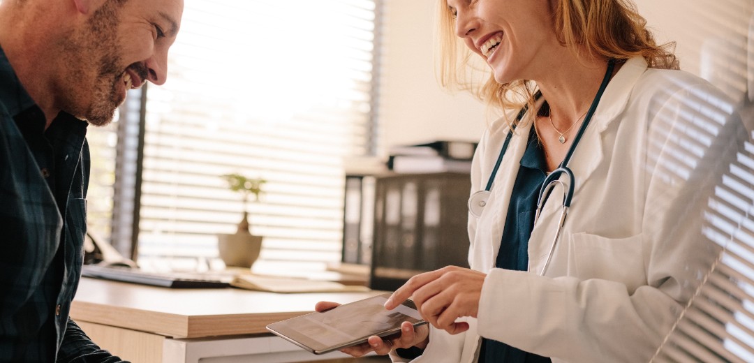 Eine Ärztin berät einen männlichen Patienten und hält ein Tablet in der Hand.