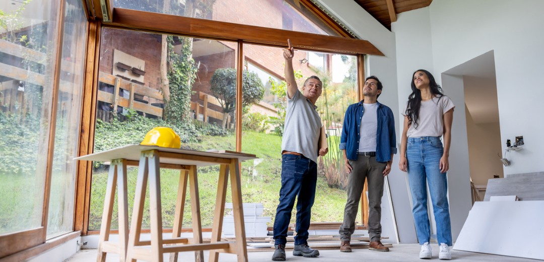 Architekt zeigt einem Paar Details bei der Besichtigung eines Hauses mit großen Fenstern.
