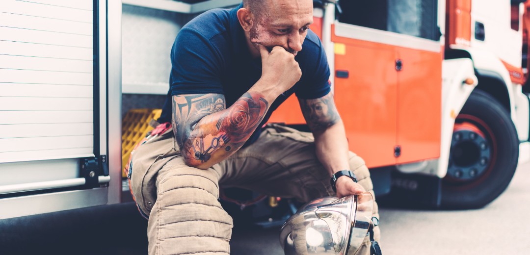 Ein erwachsener Feuerwehrmann sitzt erschöpft am Rand eines Feuerwehrautos.