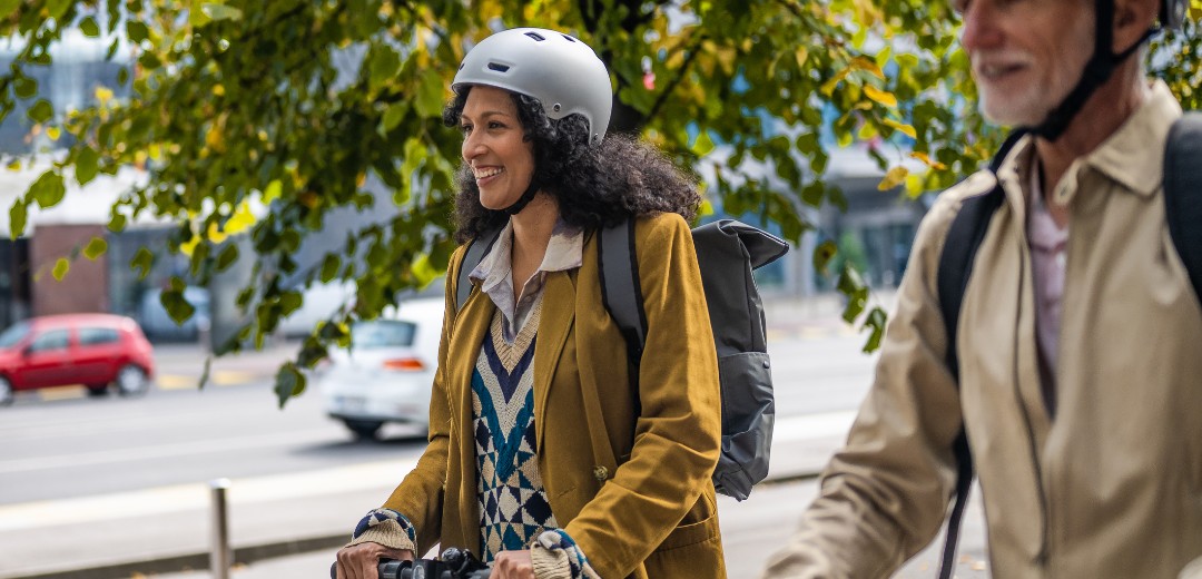 Älterer Mann fährt neben einer jüngeren Frau geschützt mit Helm E-Scooter.