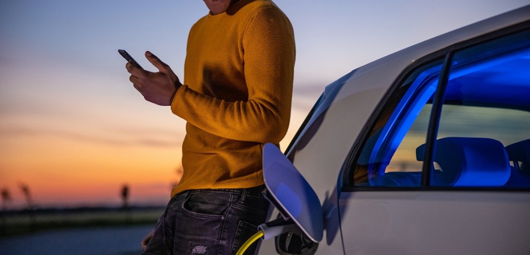 Ein junger Mann lehnt im Sonnenuntergang ein sein Elektro-Auto, während es auflädt. 