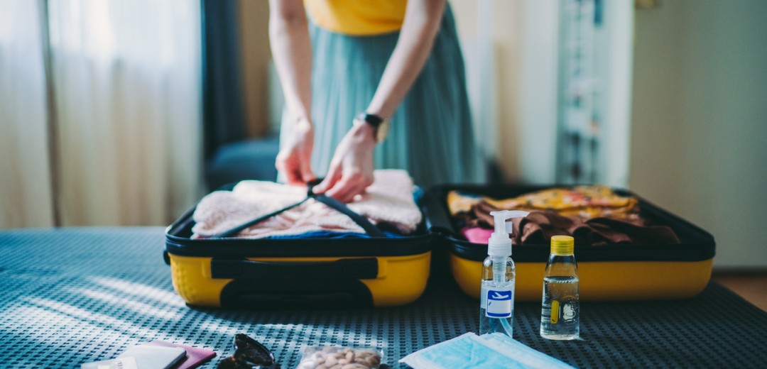 Eine Frau packt ihren Koffer auf dem Bett und hat Medikamente für die Reiseapotheke bereitgelegt. 