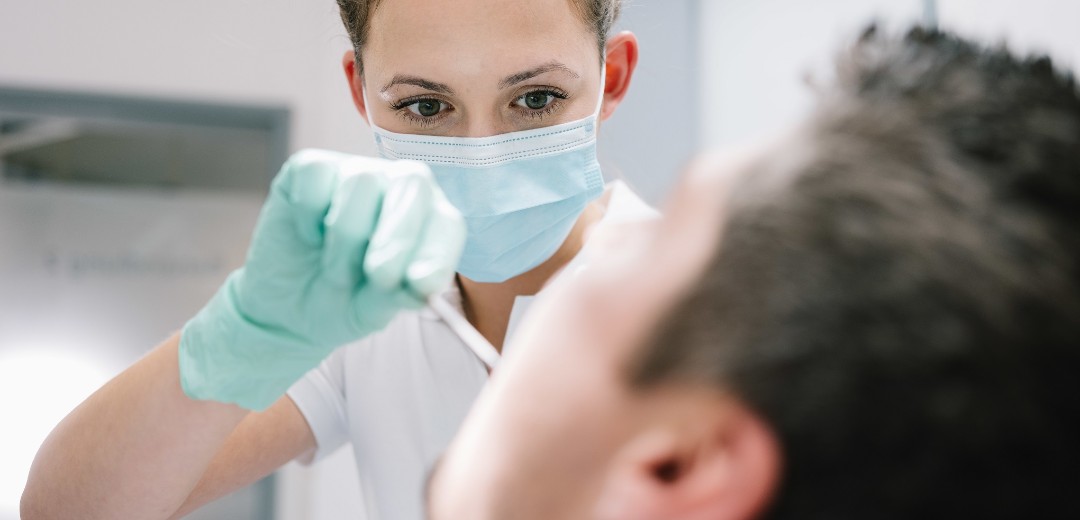 Eine Zahnärztin schaut einem Patienten in den Mund. 