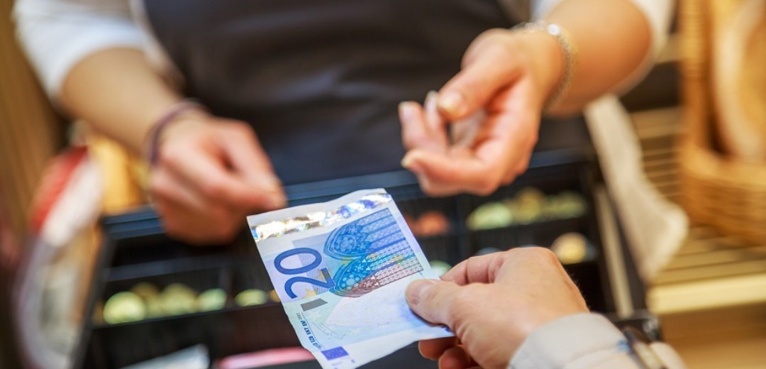 Die Hand einer Frau hält einer Kassiererin einen 20€ Geldschein hin. 