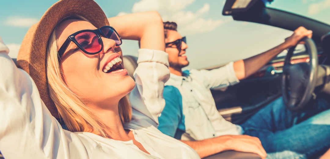 Eine Frau und  ein Mann sitzen zusammen im Cabrio und genießen das sonnige Wetter. 