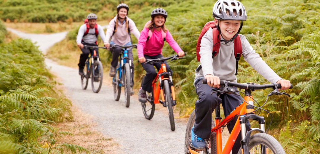 Eine Familie mit zwei Kindern fährt zusammen einen Feldweg mit dem Fahrrad entlang.