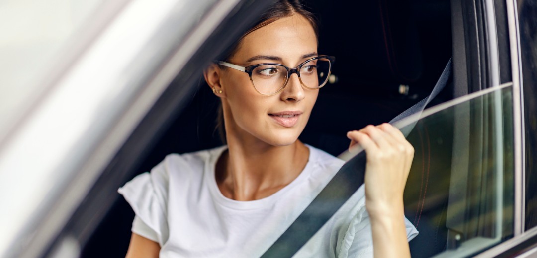 Eine junge Frau schnallt sich an und blickt dabei aus dem Autofenster.