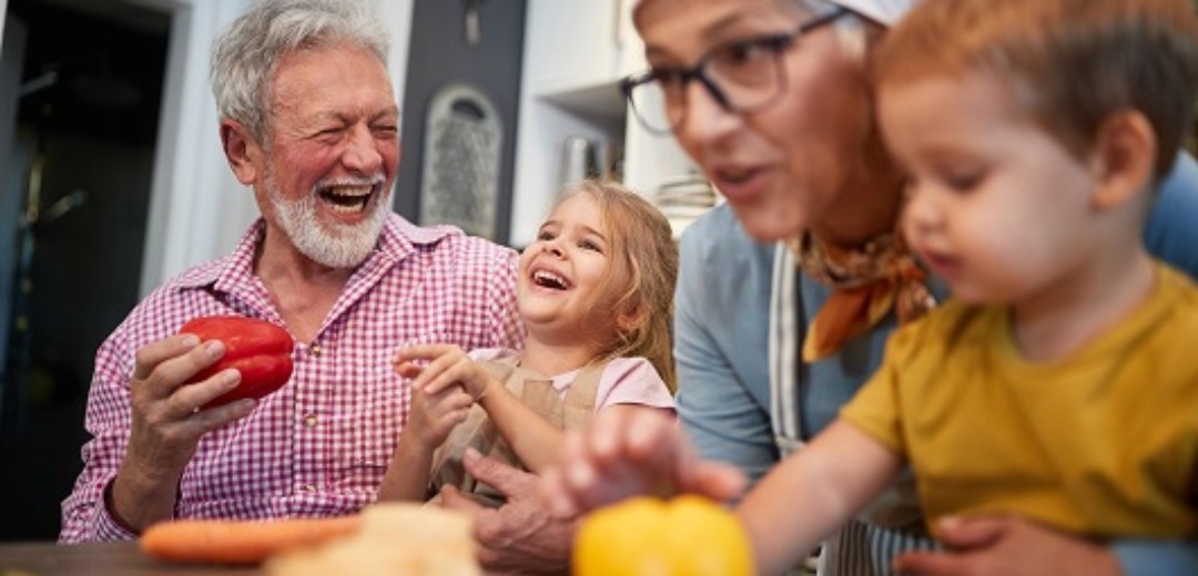 Großeltern kochen lachend gemeinsam mit ihren zwei kleinen Enkelkindern