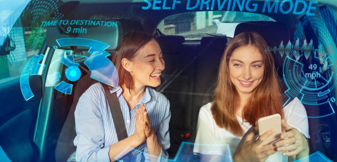 Zwei Freundinnen sitzen zusammen vorne im Auto und schauen in ein Smartphone.