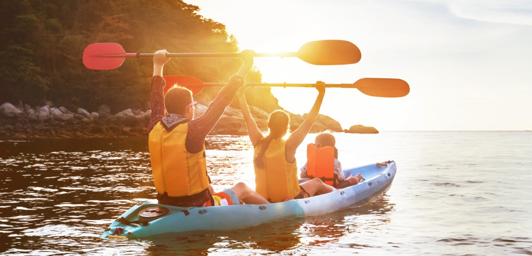 Eine dreiköpfige Familie fährt zusammen ein Kanu in der Sonne.