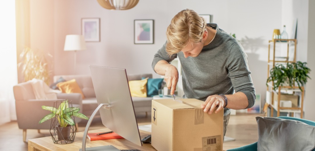 Ein Mann öffnet ein großes Paket, welches auf seinem Schreibtisch liegt. 
