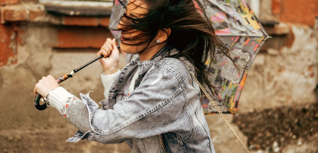 Eine Frau läuft mit ihrem Regenschirm durch einen starken Wind. Der Regenschirm hat sich bereits umgedreht. 