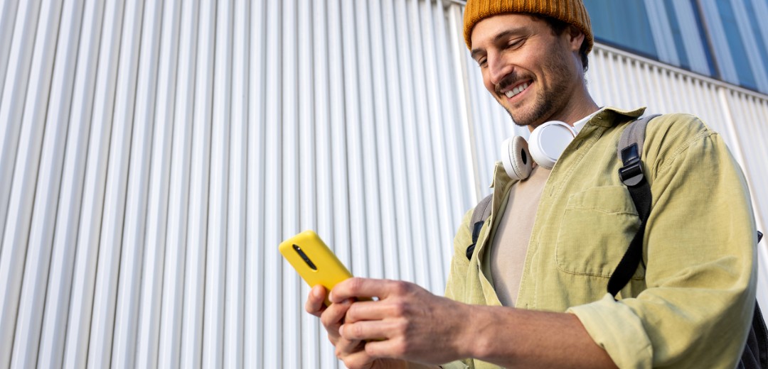 Ein junger Mann schaut beim Gehen lächelnd auf sein Handy