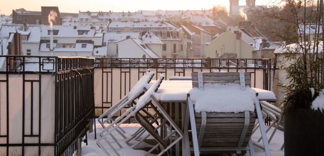 Das Bild zeigt einen Balkon mit Möbeln, die verschneit sind. 