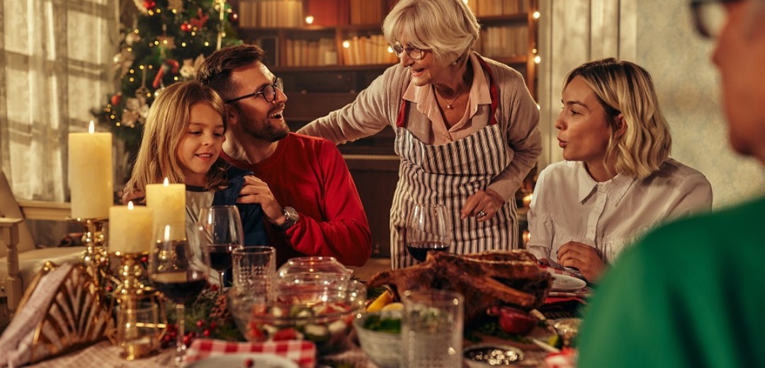 Eine Familie sitzt zusammen am Weihnachtstisch und isst. Drum herum ist es weihnachtlich geschmückt. 