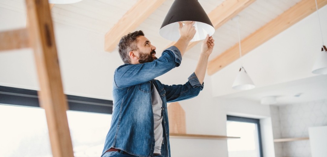 Ein Mann sitzt auf einer Leite und wechselt die Glühlampe einer Deckenleuchte. 