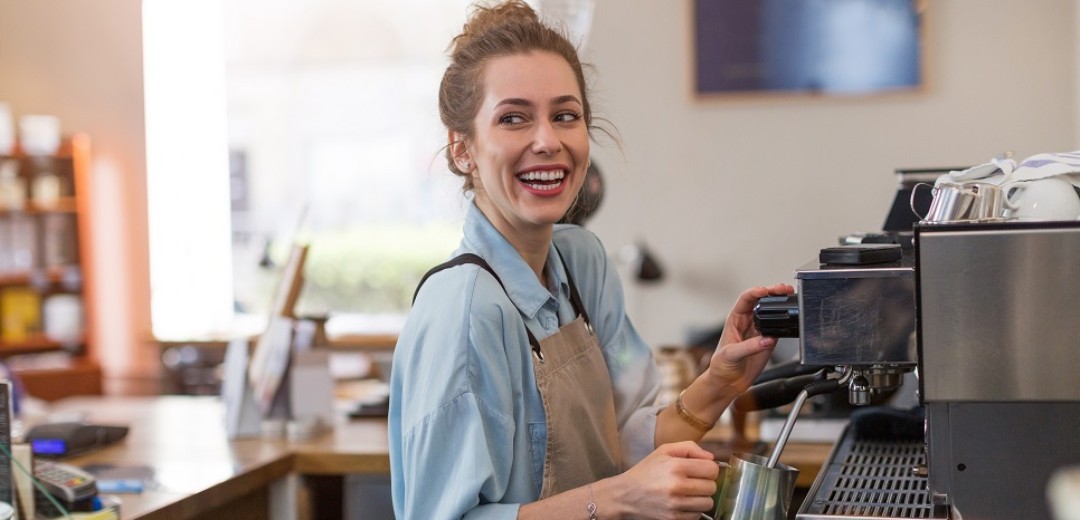 Eine junge Frau bereitet als Barista einen Kaffee an einer Kaffeemaschine in einem Café zu. 