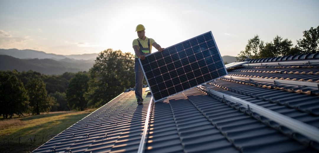 Ein Mann verlegt auf dem Dach eines Hauses Solarpanels.