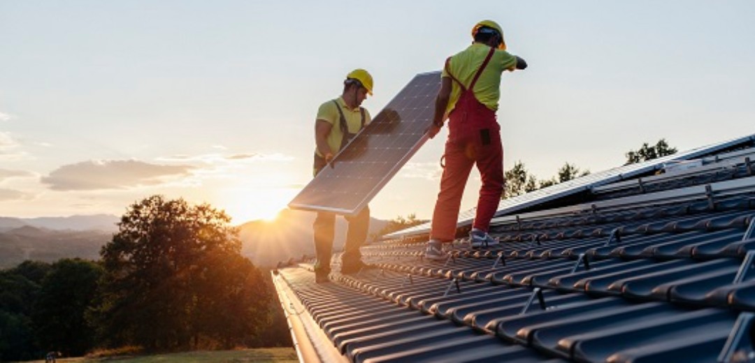 Zwei Bauarbeiter bringen eine Solaranlage auf einem Dach an.