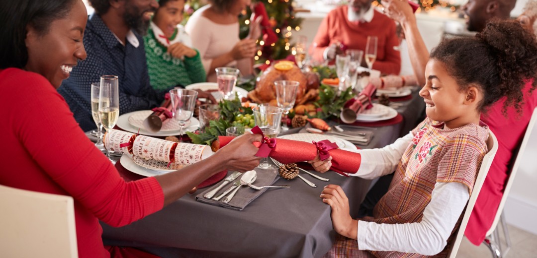 Eine mehrköpfige, dunkelhäutige Familie sitzt zusammen lachend am Weihnachtstisch. 